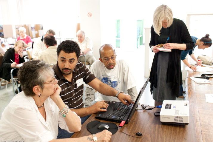 A man sits next to an elderly man and woman and points to a laptop in front of them.